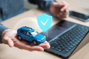A person reviews auto insurance documents at a kitchen table with a new car visible through the window.